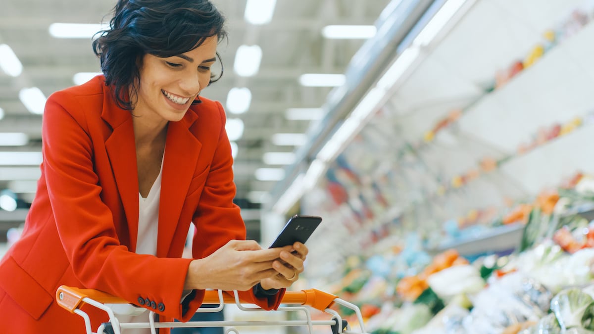 smiling woman dressed in red using her phone at the grocery store