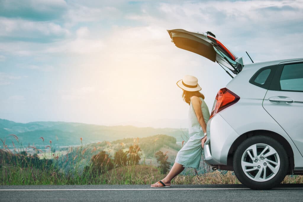 Woman traveler sitting on hatchback car with beautiful background