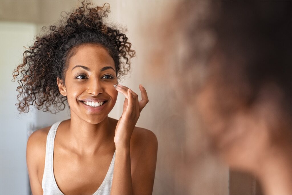 A woman smiles at her reflection in the mirror as she applies face cream