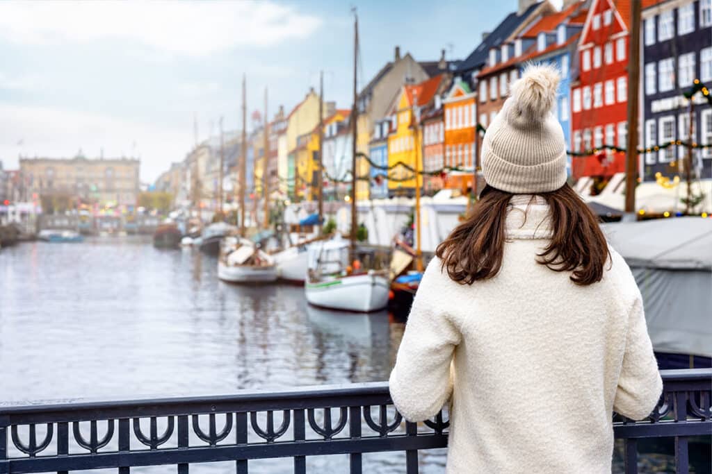 Woman wearing a sweater and warm hat looking out over a canal in a European city