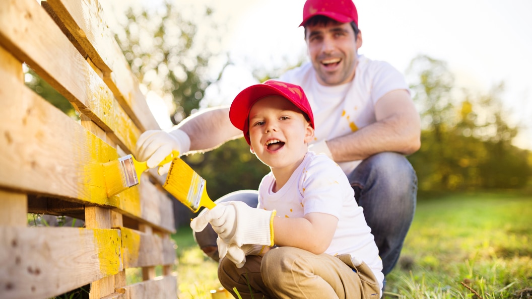 a father and son painting a wooden fence together