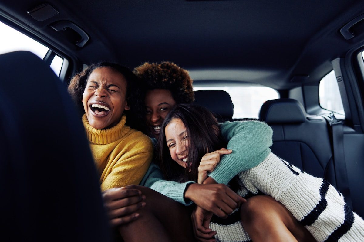 three girls having fun and laughing in the back of a car